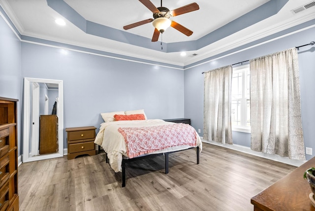 bedroom featuring a tray ceiling, visible vents, crown molding, and wood finished floors