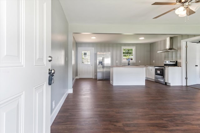 kitchen featuring a sink, white cabinetry, appliances with stainless steel finishes, wall chimney range hood, and dark wood-style floors