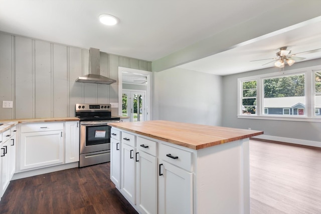 kitchen with wall chimney exhaust hood, butcher block countertops, white cabinets, and electric range