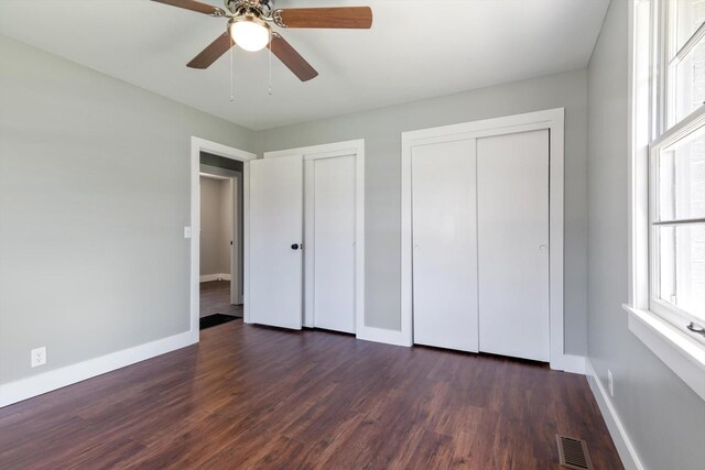 unfurnished bedroom featuring dark wood-style flooring, multiple closets, and baseboards