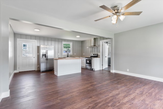 kitchen featuring baseboards, dark wood-style floors, a center island, stainless steel appliances, and wall chimney range hood