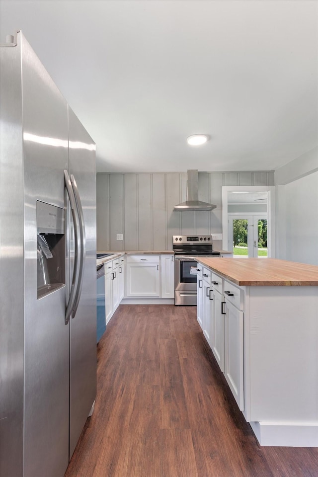 kitchen featuring dark wood-type flooring, butcher block countertops, white cabinets, appliances with stainless steel finishes, and wall chimney exhaust hood