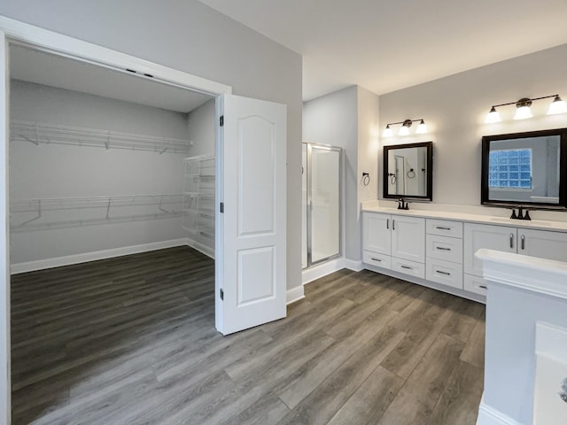 bathroom with wood finished floors, a sink, baseboards, double vanity, and a stall shower