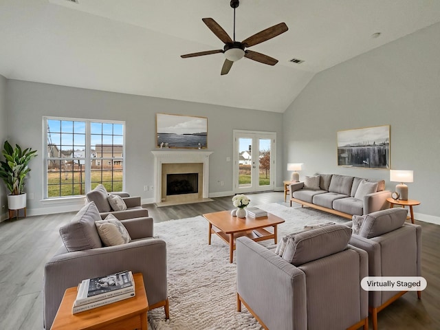 living area featuring a fireplace with flush hearth, a ceiling fan, vaulted ceiling, wood finished floors, and baseboards