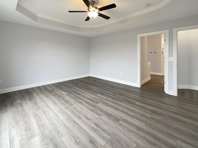 empty room featuring crown molding, dark wood finished floors, a raised ceiling, a ceiling fan, and baseboards