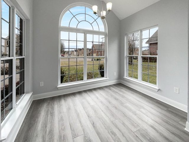 unfurnished dining area featuring an inviting chandelier, plenty of natural light, and wood finished floors