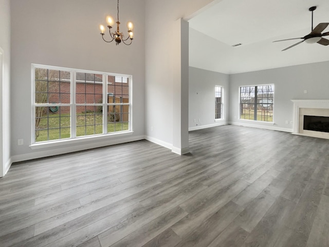 unfurnished living room featuring a fireplace, a high ceiling, wood finished floors, baseboards, and ceiling fan with notable chandelier