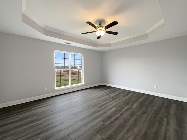 empty room featuring dark wood-type flooring, a ceiling fan, visible vents, baseboards, and a raised ceiling