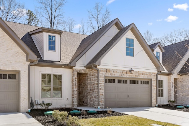 view of front of home with roof with shingles, brick siding, concrete driveway, board and batten siding, and stone siding