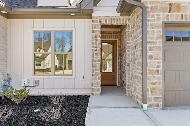 doorway to property with a garage, stone siding, board and batten siding, and roof with shingles