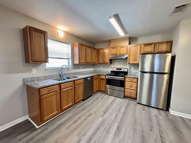 kitchen with under cabinet range hood, stainless steel appliances, a sink, visible vents, and light wood-style floors