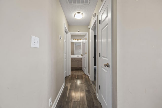 corridor featuring a textured ceiling, dark wood-style flooring, visible vents, and baseboards