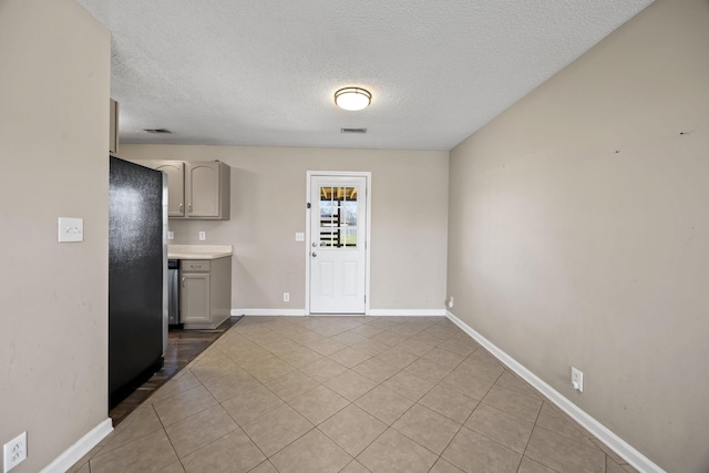 kitchen with a textured ceiling, light countertops, freestanding refrigerator, and tile patterned floors