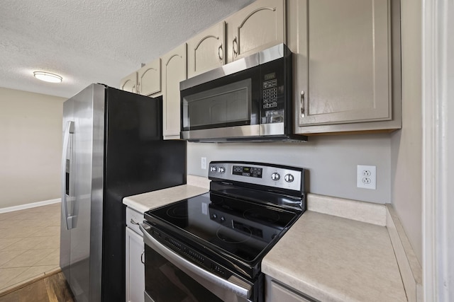 kitchen with stainless steel appliances, light countertops, a textured ceiling, dark tile patterned flooring, and baseboards