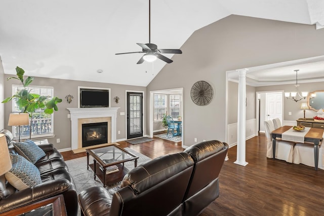 living area featuring a fireplace with flush hearth, wood finished floors, ornate columns, high vaulted ceiling, and ceiling fan with notable chandelier