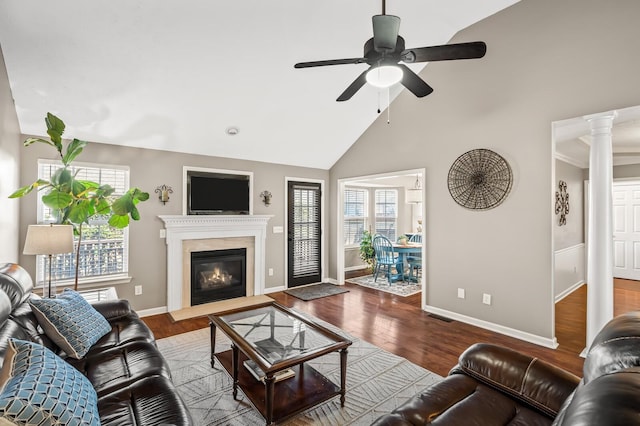 living area with decorative columns, a glass covered fireplace, ceiling fan, wood finished floors, and high vaulted ceiling