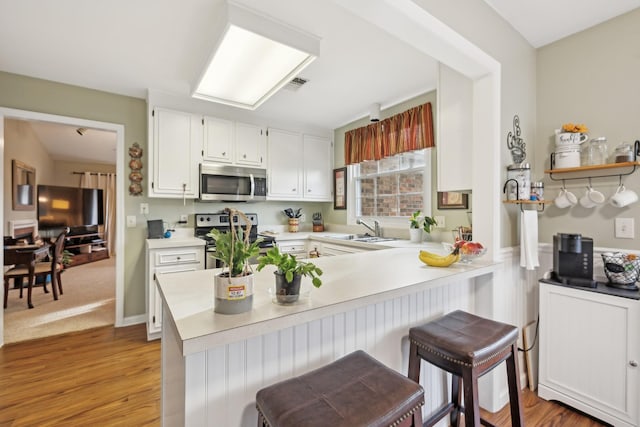 kitchen with stainless steel appliances, a peninsula, a sink, white cabinetry, and light countertops