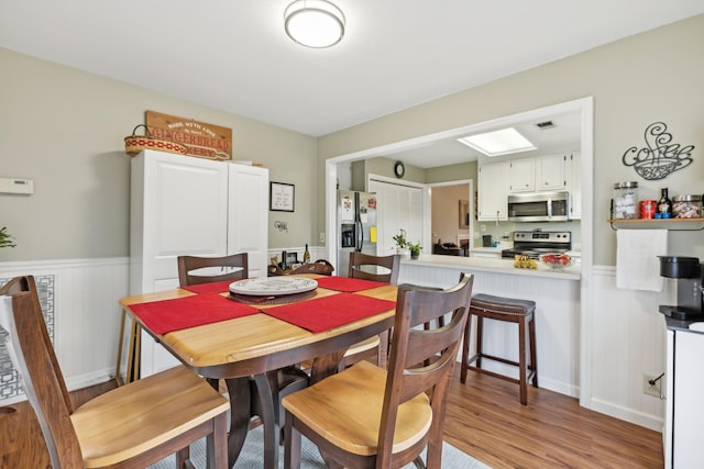 dining space featuring light wood finished floors, visible vents, and wainscoting