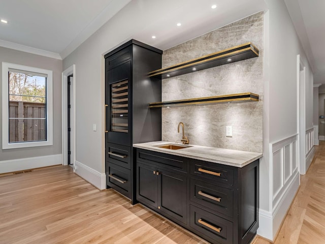 bar with indoor wet bar, crown molding, decorative backsplash, a sink, and light wood-type flooring