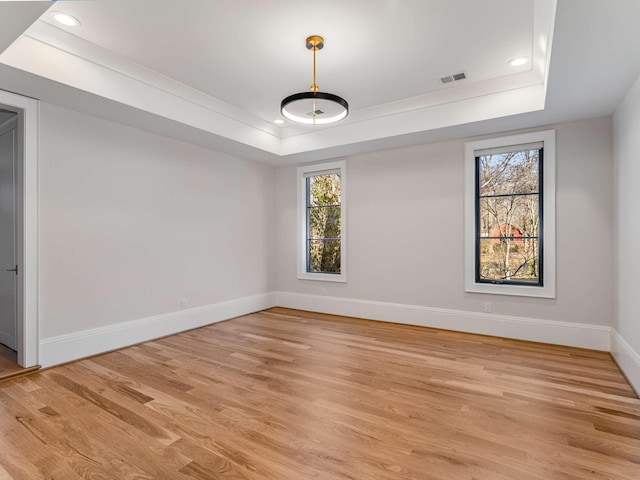 spare room with visible vents, a tray ceiling, light wood-style flooring, and baseboards