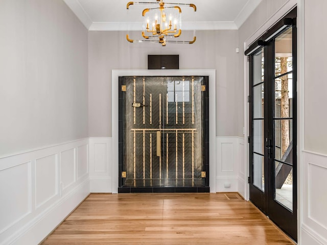 foyer entrance with ornamental molding, a decorative wall, wood finished floors, and an inviting chandelier