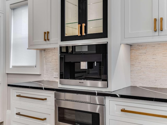 kitchen with tasteful backsplash, dark countertops, oven, and white cabinets