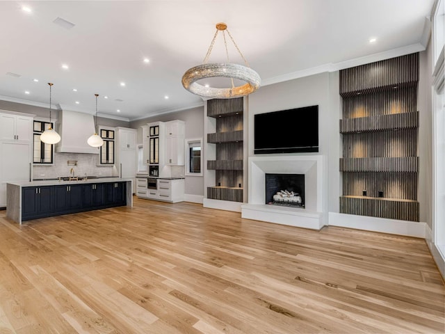 unfurnished living room featuring crown molding, recessed lighting, a fireplace with raised hearth, light wood-style flooring, and a sink