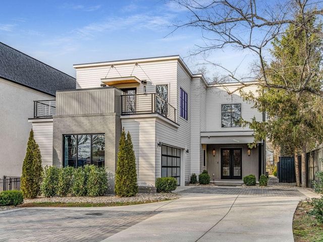 view of front of house featuring decorative driveway, french doors, an attached garage, fence, and a balcony