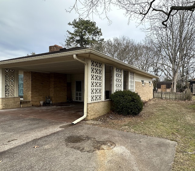 view of property exterior with a carport, brick siding, a chimney, and aphalt driveway