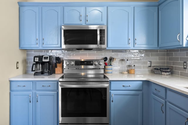 kitchen with appliances with stainless steel finishes, blue cabinets, and backsplash