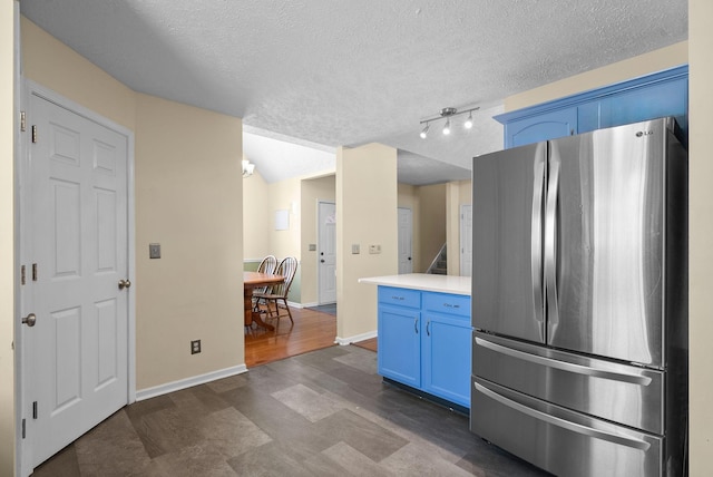 kitchen with a textured ceiling, baseboards, light countertops, blue cabinetry, and freestanding refrigerator