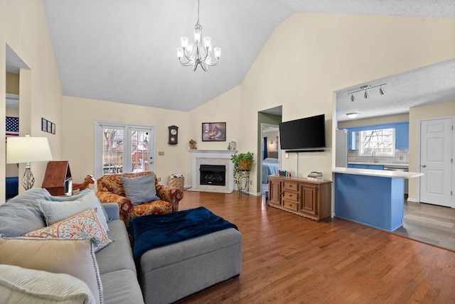 living room with high vaulted ceiling, a chandelier, a fireplace, and light wood-style flooring