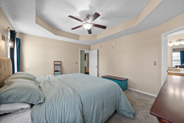 bedroom with light carpet, baseboards, a raised ceiling, ceiling fan, and a textured ceiling