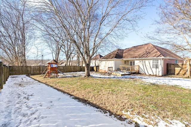 yard covered in snow featuring a playground, a fenced backyard, and a wooden deck