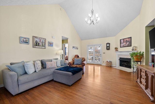 living area with baseboards, a fireplace with flush hearth, wood finished floors, high vaulted ceiling, and a notable chandelier