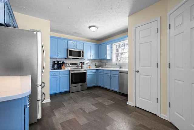 kitchen with blue cabinetry, light countertops, decorative backsplash, appliances with stainless steel finishes, and baseboards