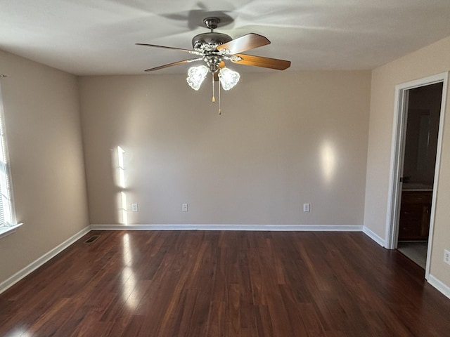 empty room with dark wood-style floors, a ceiling fan, visible vents, and baseboards