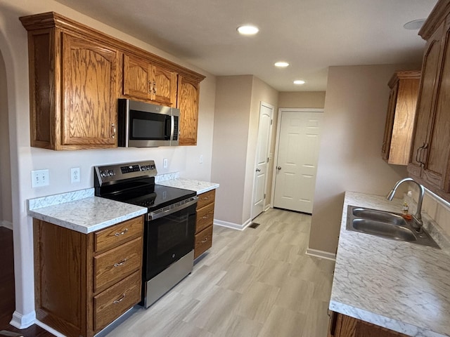 kitchen featuring a sink, baseboards, light countertops, appliances with stainless steel finishes, and light wood-type flooring