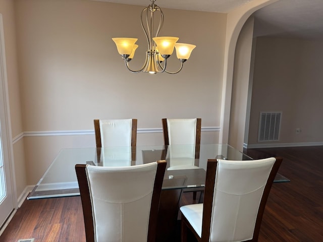 dining area featuring arched walkways, dark wood finished floors, visible vents, a chandelier, and baseboards