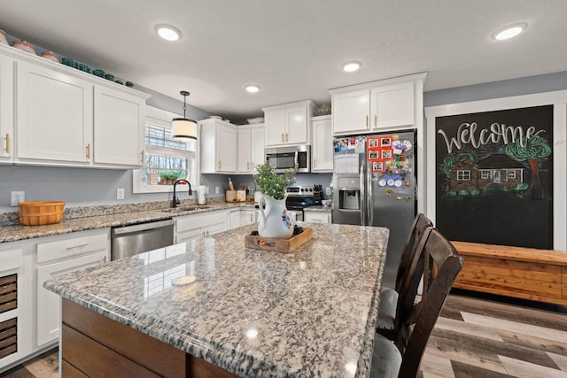 kitchen with stainless steel appliances, hanging light fixtures, white cabinetry, a sink, and a kitchen island