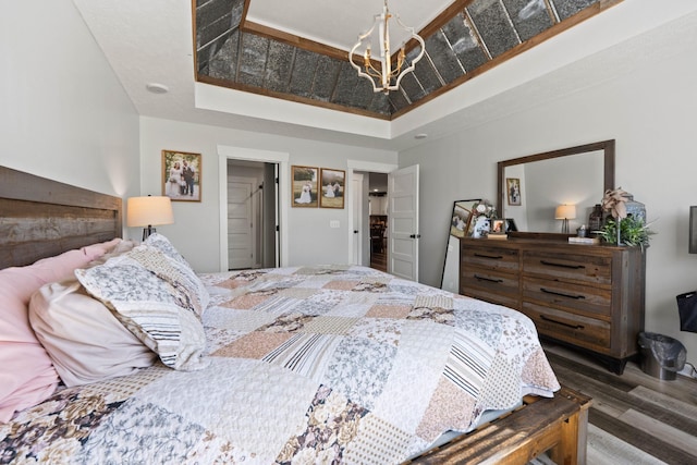 bedroom featuring an inviting chandelier, a tray ceiling, and dark wood-type flooring