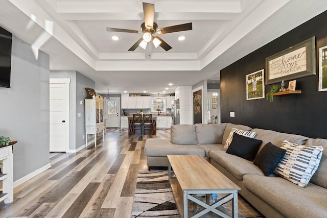 living area with a raised ceiling, ceiling fan, baseboards, and wood finished floors