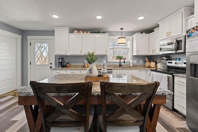 kitchen with stainless steel appliances, a sink, white cabinetry, hanging light fixtures, and light stone countertops