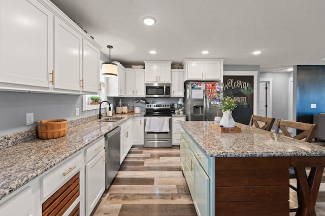 kitchen featuring a sink, a kitchen island, white cabinets, appliances with stainless steel finishes, and a kitchen bar