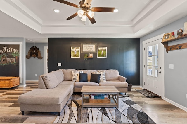 living room featuring recessed lighting, a raised ceiling, baseboards, and light wood finished floors