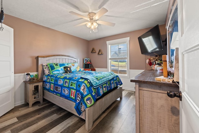 bedroom with a textured ceiling, a ceiling fan, dark wood-type flooring, and wainscoting