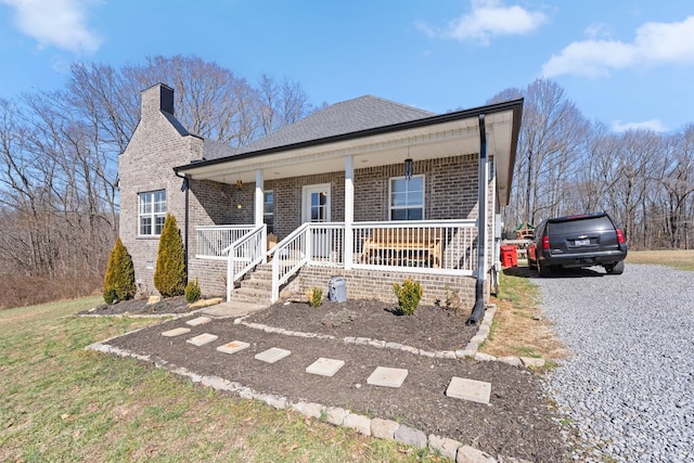 view of front facade featuring a chimney, roof with shingles, gravel driveway, covered porch, and brick siding