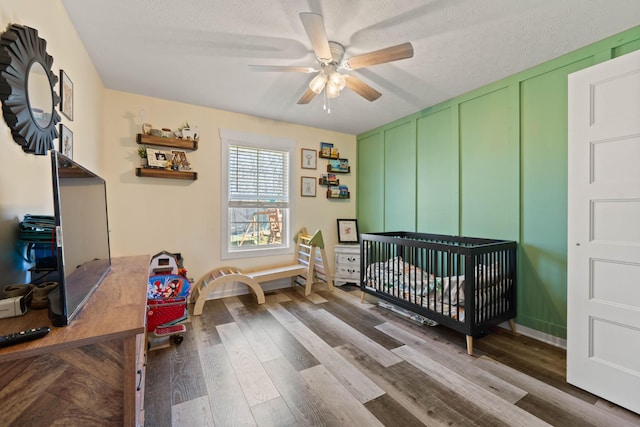 bedroom featuring a textured ceiling, a ceiling fan, a decorative wall, and wood finished floors