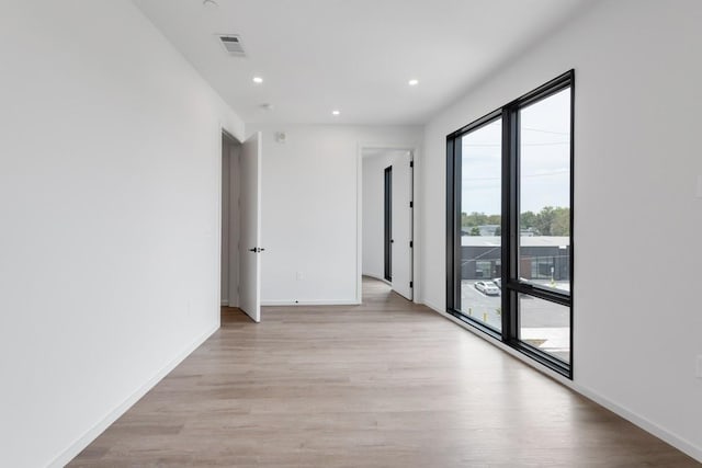 empty room featuring light wood-style floors, recessed lighting, visible vents, and baseboards