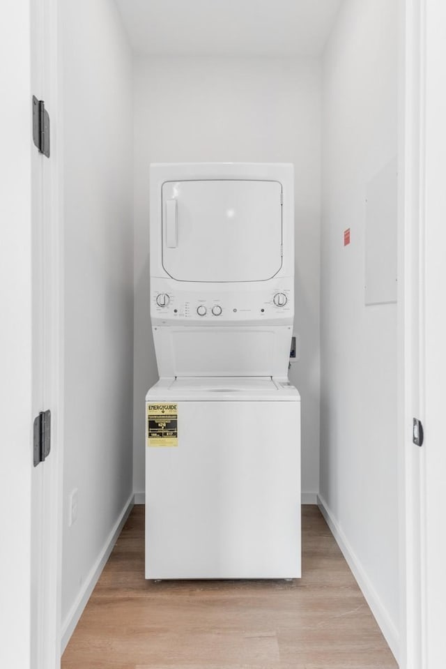 clothes washing area featuring light wood-style floors, baseboards, laundry area, and stacked washer and clothes dryer